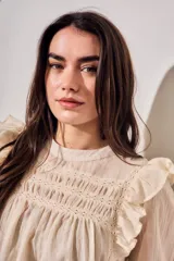 Blusa de color arena con diseño romántico, presenta volados en los hombros, detalles de encaje en el pecho y mangas largas con puños elásticos.