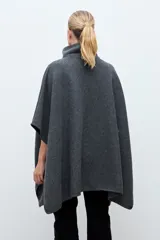 Capa de paño gris con cierre frontal y cuello alto. Presenta un diseño con paneles superiores capitoneados en la zona del pecho y hombros, y aberturas laterales para los brazos.