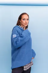 Buzo de punto azul con capucha, cierre frontal parcial y manga larga. Presenta un parche bordado con la bandera de Uruguay en la manga derecha.
