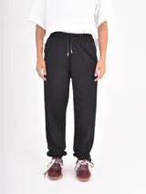 Pantalon de jogging negro de corte holgado, con cintura elastizada y cordón de ajuste frontal. Presenta puños elastizados en los tobillos.