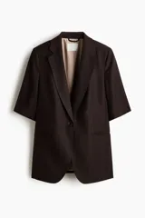 Blazer de manga corta color marrón oscuro, de botonadura sencilla con solapas de muesca, cierre de un botón, bolsillos delanteros ribeteados y forro interior.