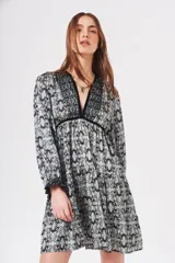 Vestido corto estampado en tonos azules, negros y beige, con escote en V profundo y ribete de terciopelo negro. Tiene mangas largas con puños fruncidos y falda con volados.