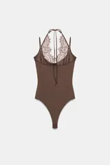 Body negro de tejido elástico con escote redondo y tirantes finos. Presenta un panel superior de encaje floral a tono con diseño halter ajustable mediante lazada en el cuello y cierre inferior con botones a presión.