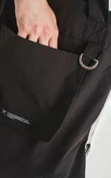 Bolso tipo tote bag de microfibra negra, con correas de hombro y cordón ajustable con tanca. Posee un bolsillo exterior con velcro y un bolsillo interior con cierre.
