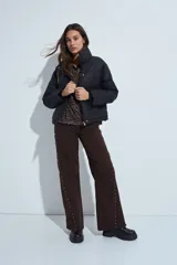 Pantalón de denim corte wide leg color marrón, con ruedo desflecado y detalle de tachas metálicas a lo largo de las costuras laterales.