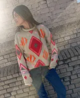 Sweater de punto color beige con diseño geométrico tejido en intarsia y detalles bordados en tonos rojo, naranja y rosado, con cuello redondo y mangas largas.