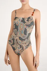 Traje de baño entero asimétrico con diseño de un solo hombro, decorado con cuentas de resina en el tirante. Presenta un estampado tipo paisley en tonos oscuros, ocres y azulados.