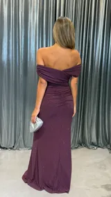 Vestido largo de fiesta color bordó con acabado brillante, diseño de escote cruzado con hombros descubiertos, detalle de frunces laterales y tajo profundo en la pierna.