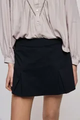 Short pollera de tiro alto confeccionado en algodón, con diseño cruzado en el delantero que simula una falda, cierre lateral invisible y bolsillos traseros.