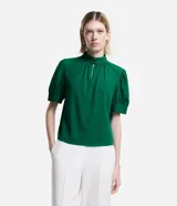 Blusa verde esmeralda de crepé con cuello alto con botones dobles y pequeña abertura abajo y mangas cortas abullonadas con botones.