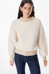 Sweater de punto grueso con diseño bicolor, cuerpo en color crema y detalles en color beige en cuello, puños y ruedo. Presenta mangas largas con caída relajada y cuello redondo.