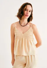 Blusa beige de tirantes finos, con escote en V y diseño fruncido tipo nido de abeja en la parte superior.