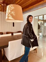 Gamulán negro con interior de corderito blanco, cuello alto, cierre frontal con broches y bolsillos laterales. Presenta tajos a los costados para mayor movilidad.