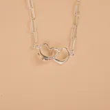 Gargantilla de cadena tipo force con eslabones alargados y dije central compuesto por dos corazones entrelazados, confeccionada en plata 925.