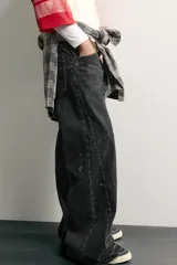 Jeans flare fit de denim de algodón negro con efecto desgastado, roturas, costuras decorativas en las perneras y bajo irregular deshilachado.