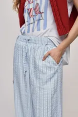 Pantalón de tiro alto con silueta amplia y caída fluida, confeccionado en tejido celeste con textura a rayas finas. Cuenta con cintura elástica con lazo de ajuste y bolsillos laterales.