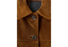 Chaqueta de cuero color marrón, con solapas clásicas, cierre frontal de botones, bolsillos aplicados en el pecho y en la parte inferior, y mangas largas.