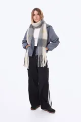 Bufanda de tejido suave y esponjoso con diseño de cuadros grandes en tonos beige, gris y amarillo, terminada con flecos en los extremos.