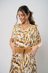 Vestido largo con estampado animal print en tonos camel, blanco y negro. Tiene escote en V, mangas cortas tipo murciélago y tajo frontal. Incluye cinturón ancho de cuero color camel.