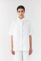 Camisa blanca de manga corta y corte recto, con cuello camisero clásico y cierre frontal de botones.