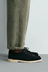 Zapato casual de cordones para hombre, confeccionado en piel con acabado serraje de color negro. Presenta detalle de bordón en el empeine, horma redonda y suela plana en contraste de color beige.