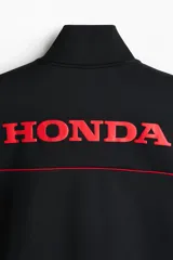 Campera deportiva negra de efecto neopreno con cierre bidireccional, cuello elevado y bolsillos laterales. Presenta detalles de ribetes rojos en el pecho y el logo de Honda bordado en rojo.