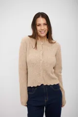 Saco tipo cardigan de punto, color beige, con cierre frontal de botones y terminaciones onduladas en el ruedo y puños.