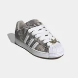 Championes Adidas Superstar ST de estilo skate, con exterior estampado en animal print de serpiente en tonos grises y tostados, las icónicas tres tiras blancas en los laterales y la clásica puntera de concha de goma blanca. Cuentan con cordones anchos blancos, lengüeta acolchada y suela chunky blanca con detalles marrones.