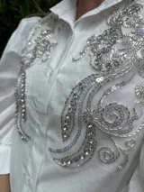 Camisa blanca de mangas 3/4 con bordados de lentejuelas y mostacillas plateadas en el frente.