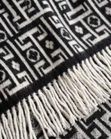 Poncho de lana negro y blanco con diseño geométrico y flecos en el borde inferior.