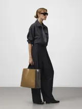 Bolso shopper de estructura cuadrada en color marrón con acabado brillante y textura craquelada. Cuenta con asas de mano y asa larga para hombro en color negro, cierre de solapa interior con cremallera y bolsillo interior. Logo grabado en la parte frontal.