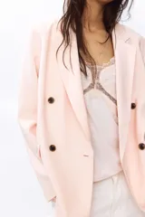 Blazer rosado de doble botonadura levemente largo con hombreras, solapas de muesca, bolsillos delanteros ribeteados con solapa y forro interior.