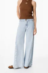 Jean color beige de corte recto, con detalles de costuras deshilachadas en los laterales y etiqueta de cuero marrón con el logo "PETRA" en la parte trasera de la cintura.