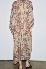 Vestido tipo túnica de viscosa con escote en pico y mangas tipo capa. Presenta un diseño estampado con motivos ornamentales en tonos tierra, beige y rosado, con pliegues en la cintura y bajo asimétrico.