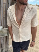 Camisa de manga corta confeccionada en tejido de punto con textura calada en patrón de espiga. Presenta cuello solapa, cierre frontal con botones y corte recto.