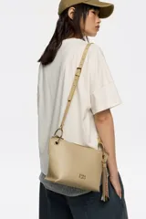 Bolso bandolera de estructura rígida y tamaño mediano confeccionado en piel vacuna. Presenta asa regulable, cierre con cremallera, bolsillo interior y logo metálico de la marca. Incluye un charm decorativo con borlas en el lateral y acabados metálicos.