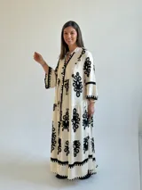 Vestido largo color marfil con estampado ornamental en color negro, escote en V con botones frontales, mangas largas amplias y diseño escalonado en la falda.