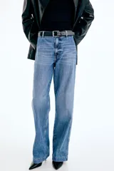 Pantalón de jean de tiro alto con corte wide leg, confeccionado en denim de algodón rígido. Presenta cierre frontal con doble botón, pasacintos y pliegues marcados en la parte delantera y trasera.
