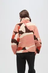 Buzo de polar tipo canguro con cuello alto y cierre frontal parcial. Presenta un diseño estampado con bloques de colores en tonos rosado, naranja, marrón y crema, y cuenta con un bolsillo frontal con cierre en contraste de color marrón.
