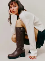 Bota de caña alta estilo biker, confeccionada en cuero negro. Presenta tres hebillas metálicas decorativas, cierre lateral y taco de madera.