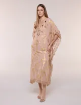Vestido midi tipo túnica de silueta holgada, marca America & Beyond, color rosado con estampado metalizado dorado de palmeras. Cuenta con escote en V, detalles de borlas, espejos y apliques decorativos, y flecos en mangas, laterales y ruedo.