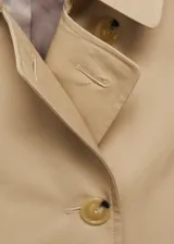 Trench coat de corte recto y diseño cruzado, confeccionado en algodón con acabado repelente al agua. Presenta cuello de solapa, cierre frontal con botones efecto carey, cinturón ajustable en la cintura, trabillas en los puños y abertura posterior en el bajo.