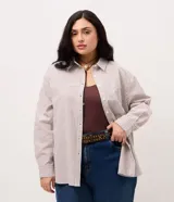 Camisa plus size alargada de Ashua, confeccionada en tela anarruga con diseño a rayas en tonos marrón y blanco. Presenta cuello inglés, cierre frontal con botones y mangas largas.