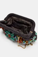 Bolso de mano negro con cuerpo cubierto de abalorios y apliques florales multicolores. Asa de anillas metálicas extraíble en forma de bandolera. Bolsillo interior y forro interior. Cierre mediante clip.