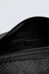 Bolso tipo bowling color negro con textura geométrica en relieve. Tiene doble asa de mano y correa de hombro ajustable y extraíble. El compartimento principal tiene cierre de cremallera y un bolsillo interior con cremallera.