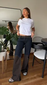Pantalón de jean de tiro medio con diseño bicolor, combinando un tono azul oscuro en la parte superior y un tono más claro en la parte inferior. Presenta una cintura con detalle de textura tipo animal print y costuras reforzadas en las rodillas.