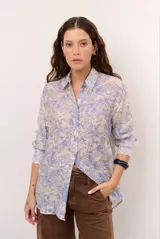 Camisa de seda color celeste y beige, con estampado de hojas en tonos azules, cuello camisero, manga larga y cierre frontal de botones.