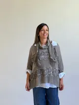 Sweater de punto color visón con diseño superpuesto, que incluye una bufanda integrada y detalles de encaje floral en el frente. Presenta mangas tres cuartos con puños abotonados y un corte holgado.