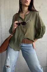 Camisa verde de tejido liviano, con cuello romántico con volados, mangas abullonadas tres cuartos con puños fruncidos y cierre frontal con botones.
