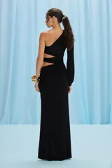 Vestido largo negro de jersey, con diseño de un solo hombro y manga larga abullonada. Presenta un detalle de hebilla en el escote, aberturas cut-out estratégicas en el corpiño y una falda fluida con una abertura cruzada en la parte delantera. Se cierra con una cremallera invisible en el lateral.